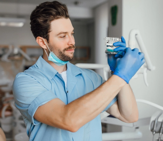 Male dental professional wearing blue gloves and scrubs examining a dental model in a clinic.